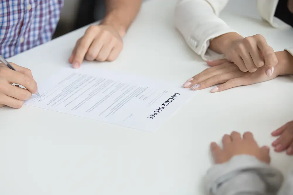 Person signing a divorce decree at a table, other hands resting nearby