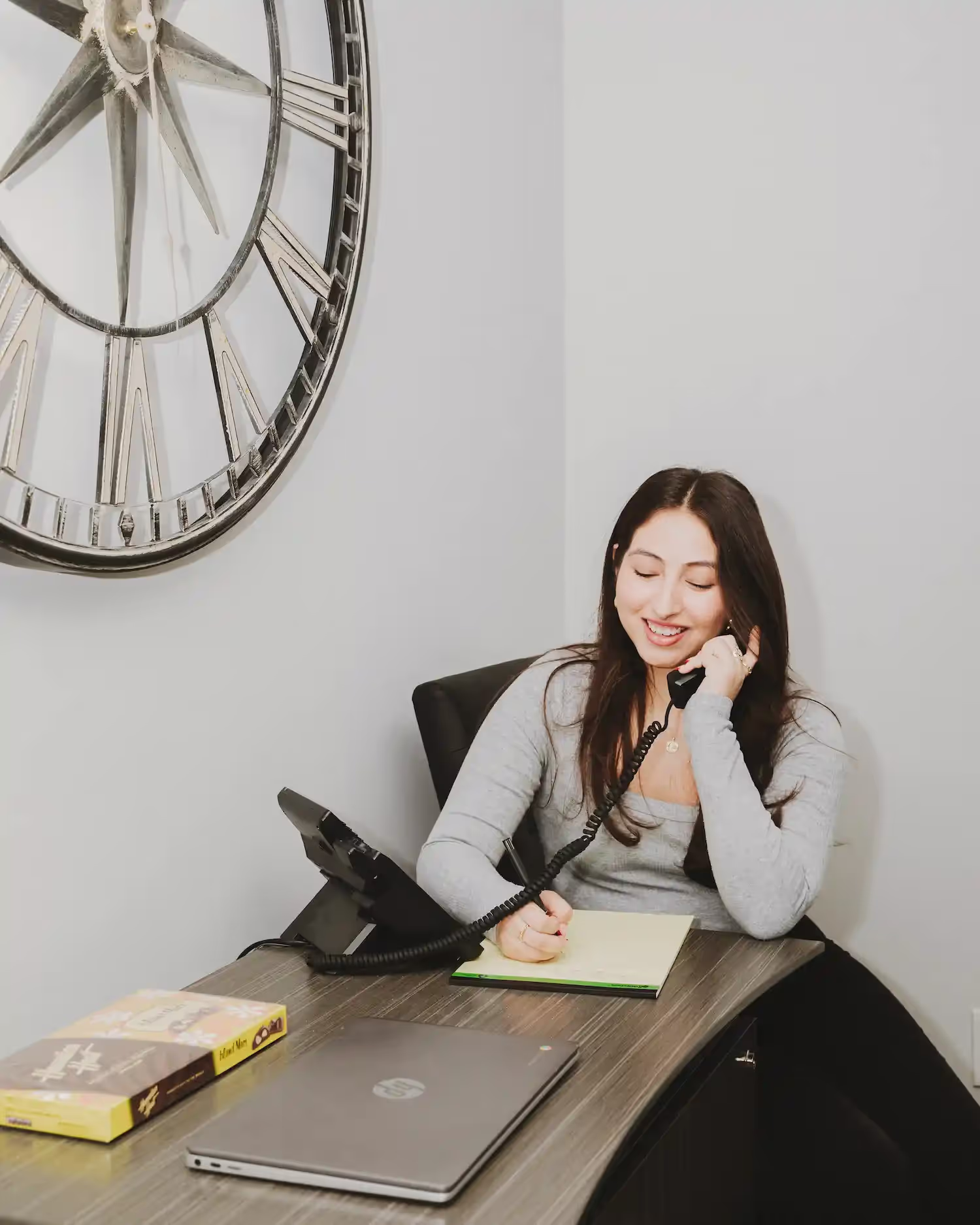 A smiling woman on the phone at her desk, taking notes